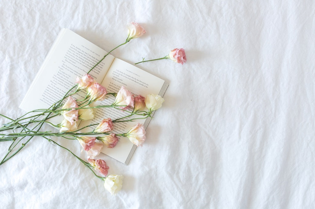 Bedlinnen waarop bloemen en een leesboek liggen.