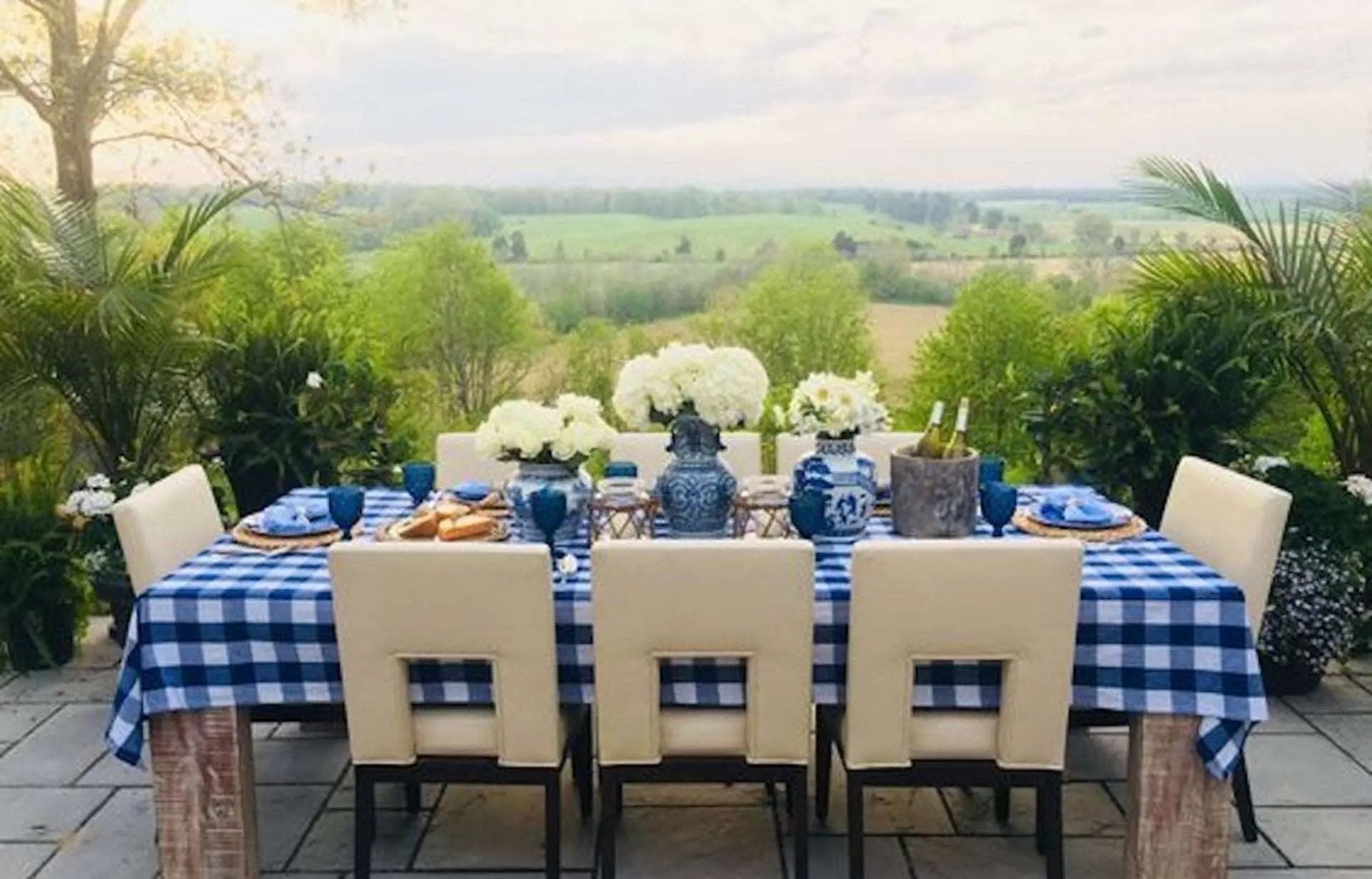 Gedekte tuintafel met blauw wit geruit tafelkleed en servetten met uitzicht over het landschap - Bamar Lifestyle